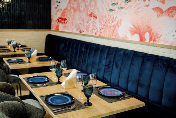 Un restaurante con largas mesas de madera, asientos tapizados en azul y detalles decorativos con motivos florales.
