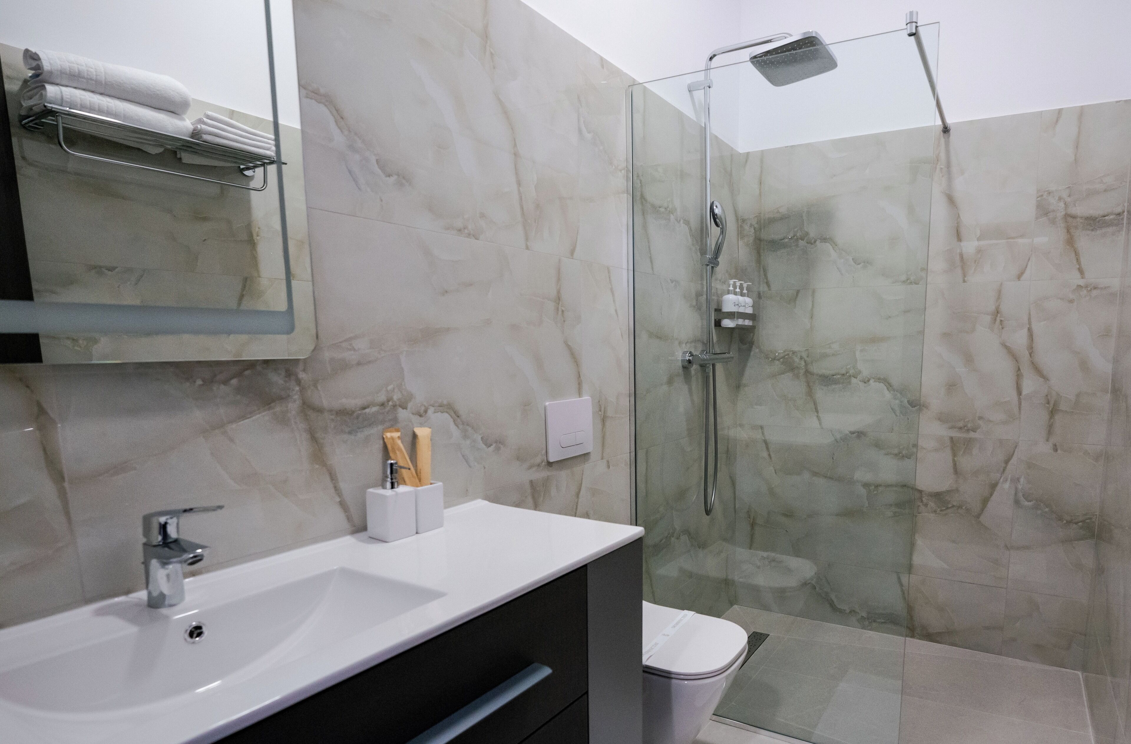 A modern bathroom with a glass-enclosed shower, a white sink, and marble walls.
