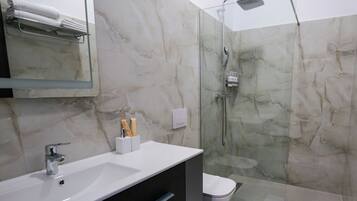 A modern bathroom with a glass-enclosed shower, a white sink, and marble walls.