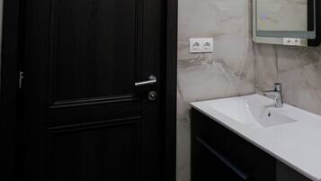 A dark wooden door with a silver handle, a white sink with a modern faucet, and a marble wall with a mirror above it.