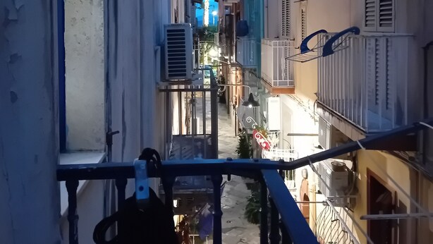 A narrow urban street with buildings on both sides, a pedestrian pathway, and a view of a distant street with lights. - Lovely Sea (Gaeta)