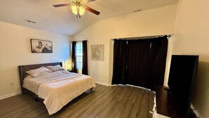 Ein Schlafzimmer mit Bett, Deckenventilator, Fenster mit Vorhängen und einem Fernsehschrank.
