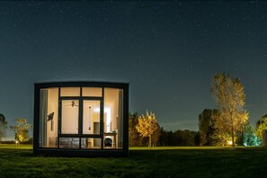 En moderne hytte med glasvægge, ventilator, spiseplads og åbent køkken.