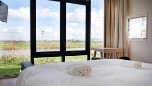 A hotel room with a large bed, a view of a river and fields, and a small table. - Leien Tiny House in Weidum (Weidum)