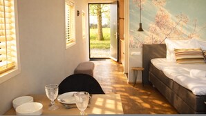 A bedroom with a bed, a table with glasses, a bench, and a door leading to a garden. - Geau Tiny House in Weidum (Weidum)