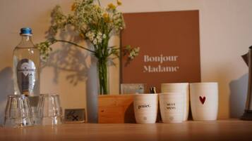 A table with a bottle, glasses, a vase with flowers, and a sign saying "Bonjour Madame".