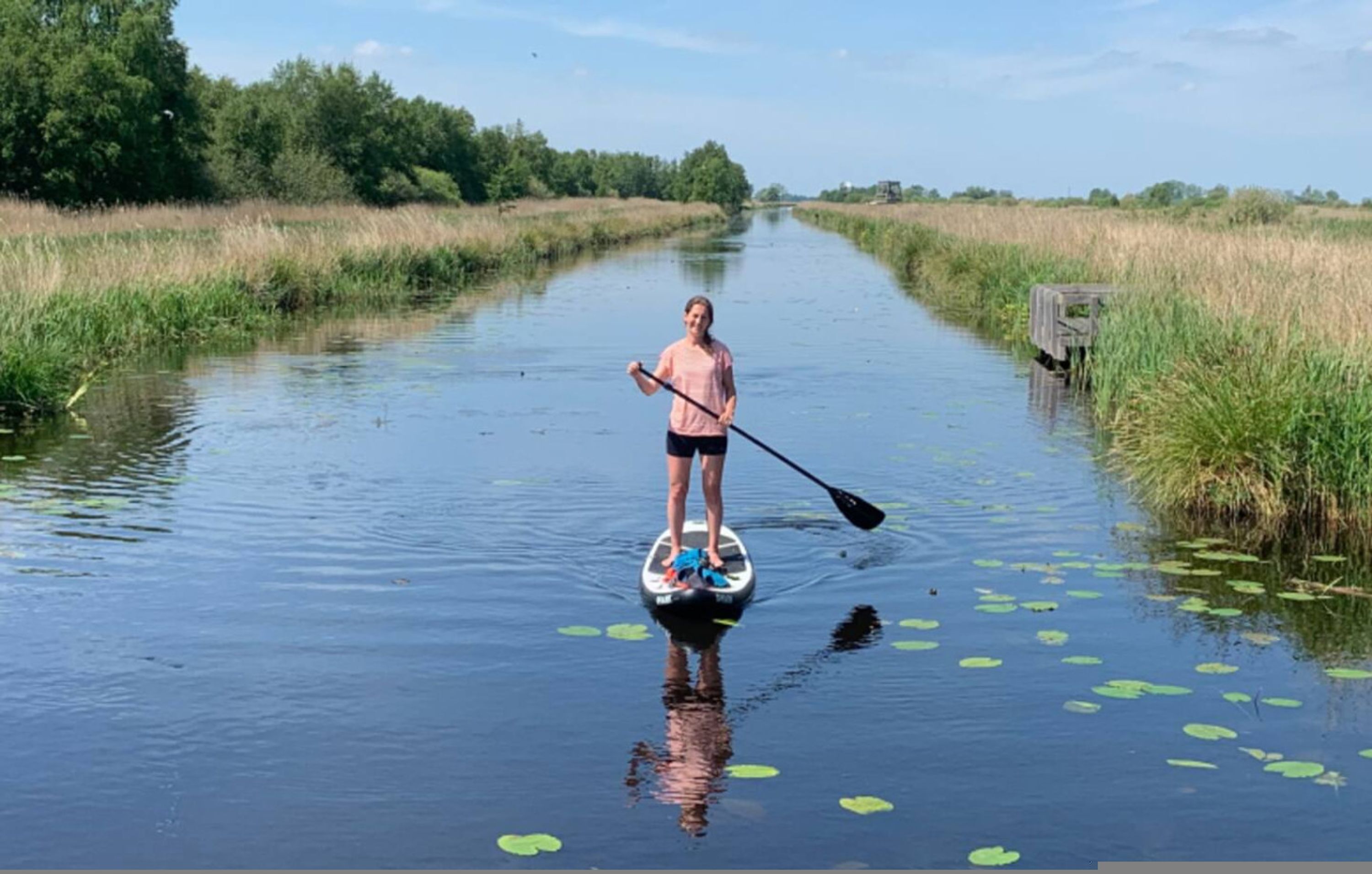 A person paddleboarding on a calm waterway surrounded by lush greenery.