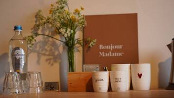 A table with a bottle, glasses, a vase with flowers, and a sign that reads 'Bonjour Madame'.