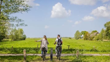 Two people on bicycles on a rural path with greenery and a house in the background.
