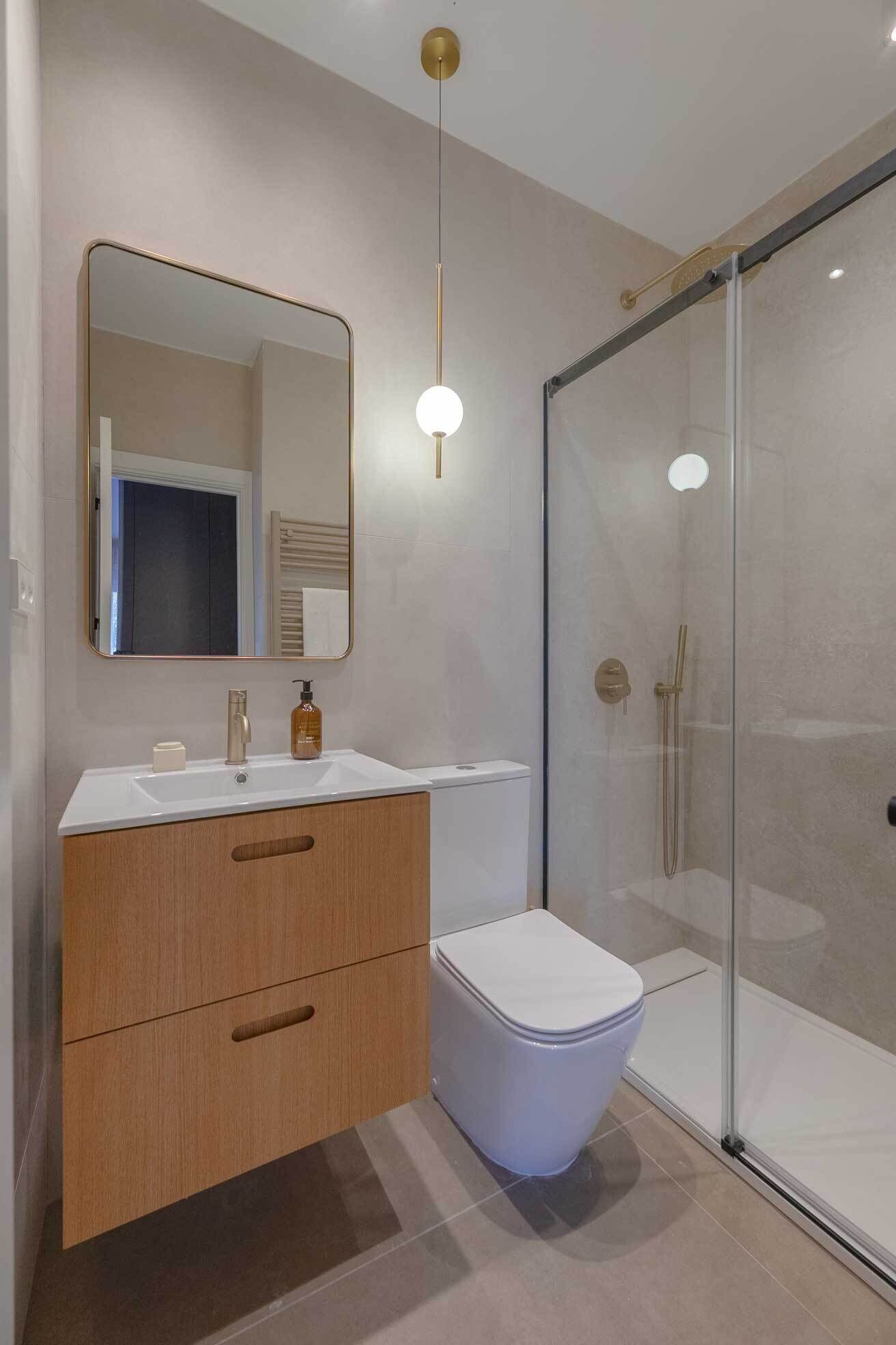 A modern bathroom with a white sink, wooden vanity, a toilet, and a glass shower enclosure.