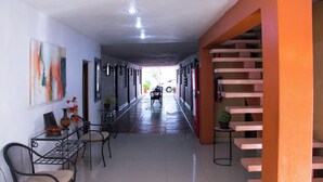 A corridor with a staircase on the right, a table with chairs and a vase on the left, and a painting on the wall. - Hotel Posada del Ángel (Mérida)