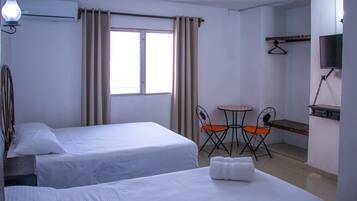 Habitación de hotel con dos camas, una pequeña mesa con sillas, un televisor montado en la pared y una ventana con cortinas.