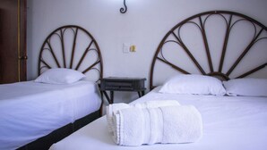 Two single beds with white linens, a small bedside table, and a wall-mounted light fixture. - Hotel Posada del Ángel (Mérida)