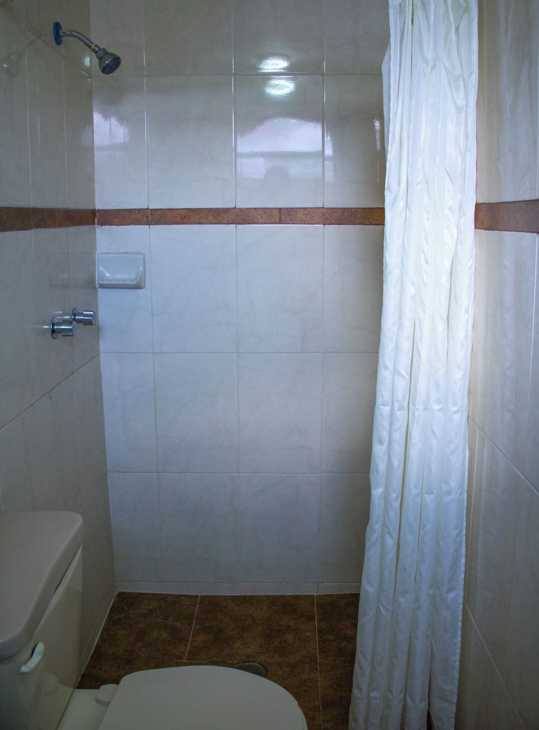 Un baño pequeño con azulejos, un inodoro, ducha y una cortina blanca.
