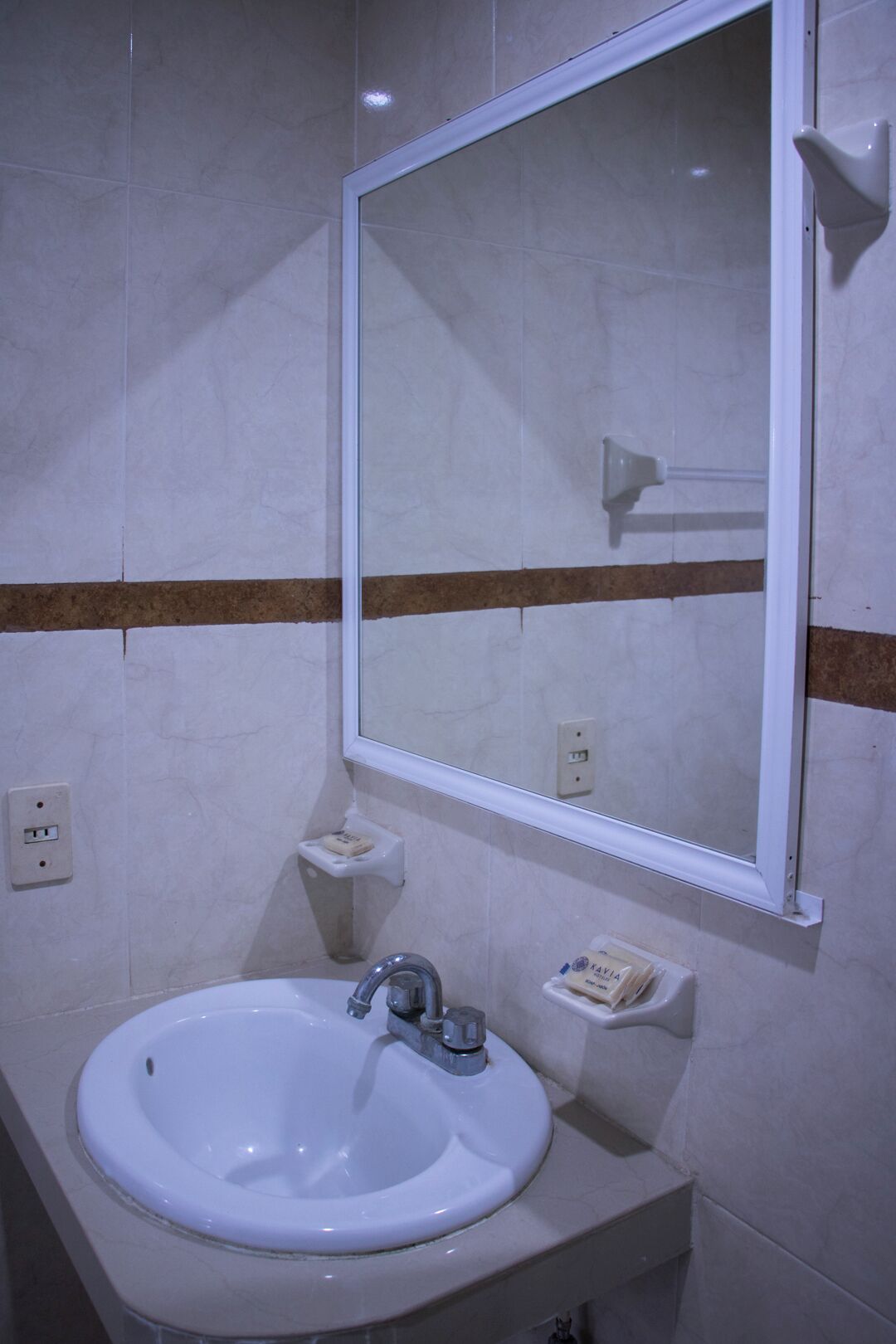 A bathroom with a white sink, a mirror, and a soap dispenser on the wall.