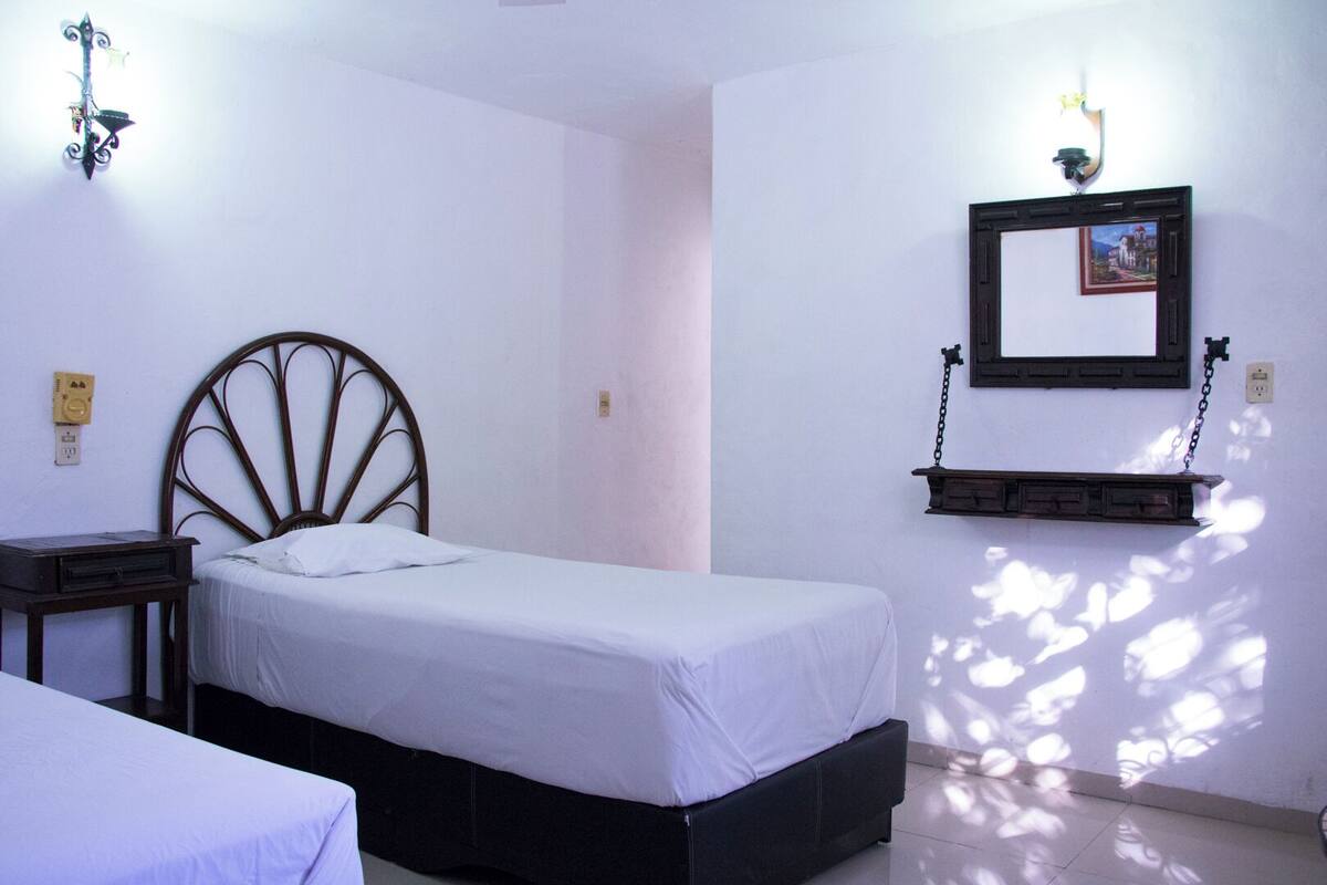 A bedroom with a single bed, a bedside table, a wall-mounted shelf, and a wall-mounted light fixture.