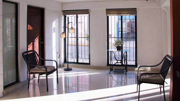 A spacious room with a ceiling fan, two large windows with metal bars, a small table with a potted plant, and two chairs. - Hotel Posada del Ángel (Mérida)