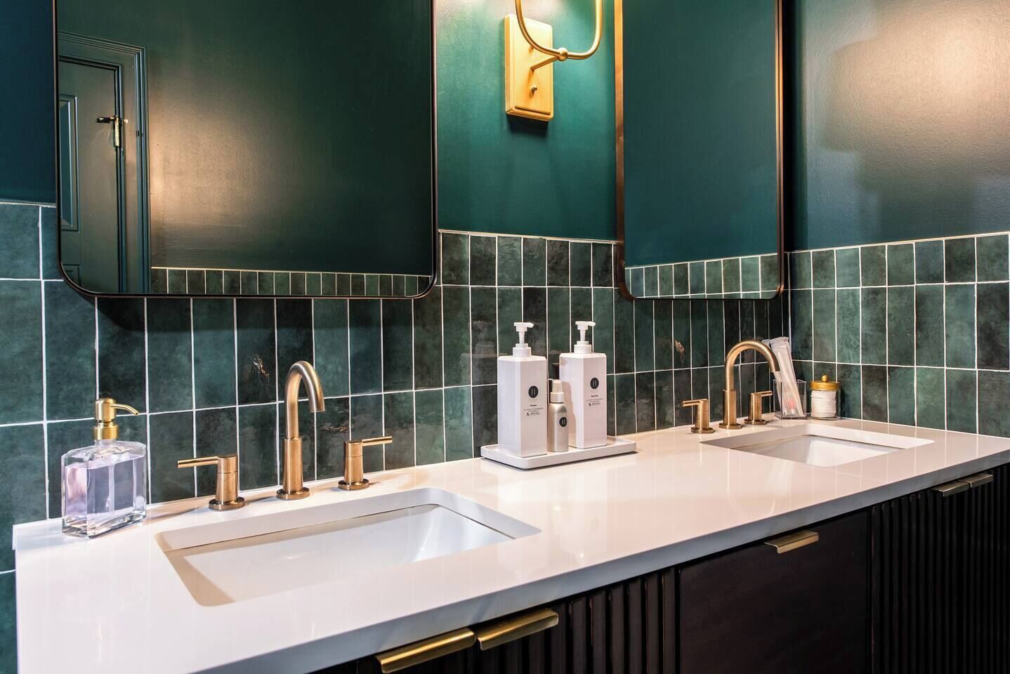 A modern bathroom with two sinks, gold faucets, and a mirror above each.