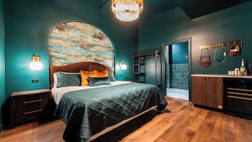 A bedroom with a large bed, a wooden headboard, a wall-mounted shelf, a vanity with a mirror, and a hanging bag.