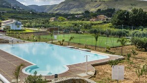 Una piscina amb una zona de solàrium al voltant, una pista de tennis i un paisatge de muntanyes al fons.