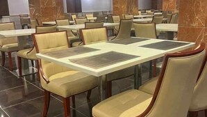 Ένας ευρύχωρος χώρος τραπεζαρίας με πολλά τραπέζια και καρέκλες, μαρμάρινα κιονόσταια και πλακάκια στο δάπεδο.