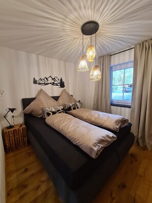 Un dormitorio con cama, lámpara de pared, ventana con cortinas y un adorno en la pared.