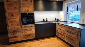 A modern kitchen with wooden cabinetry, a built-in oven, and a window overlooking a parking area. - Allgäu 17 – Modern Alpine-Style Apartment (Leutkirch im Allgäu)