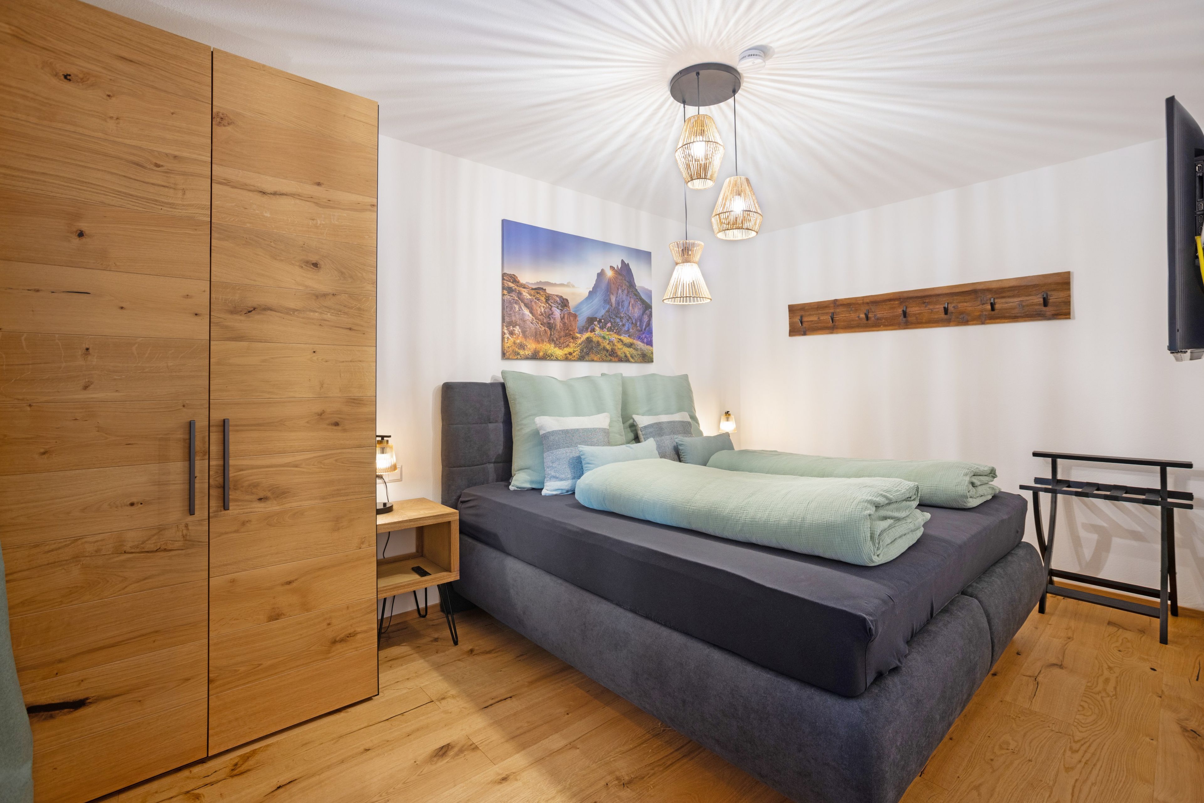A bedroom with a bed, wooden wardrobe, and a wall-mounted shelf.
