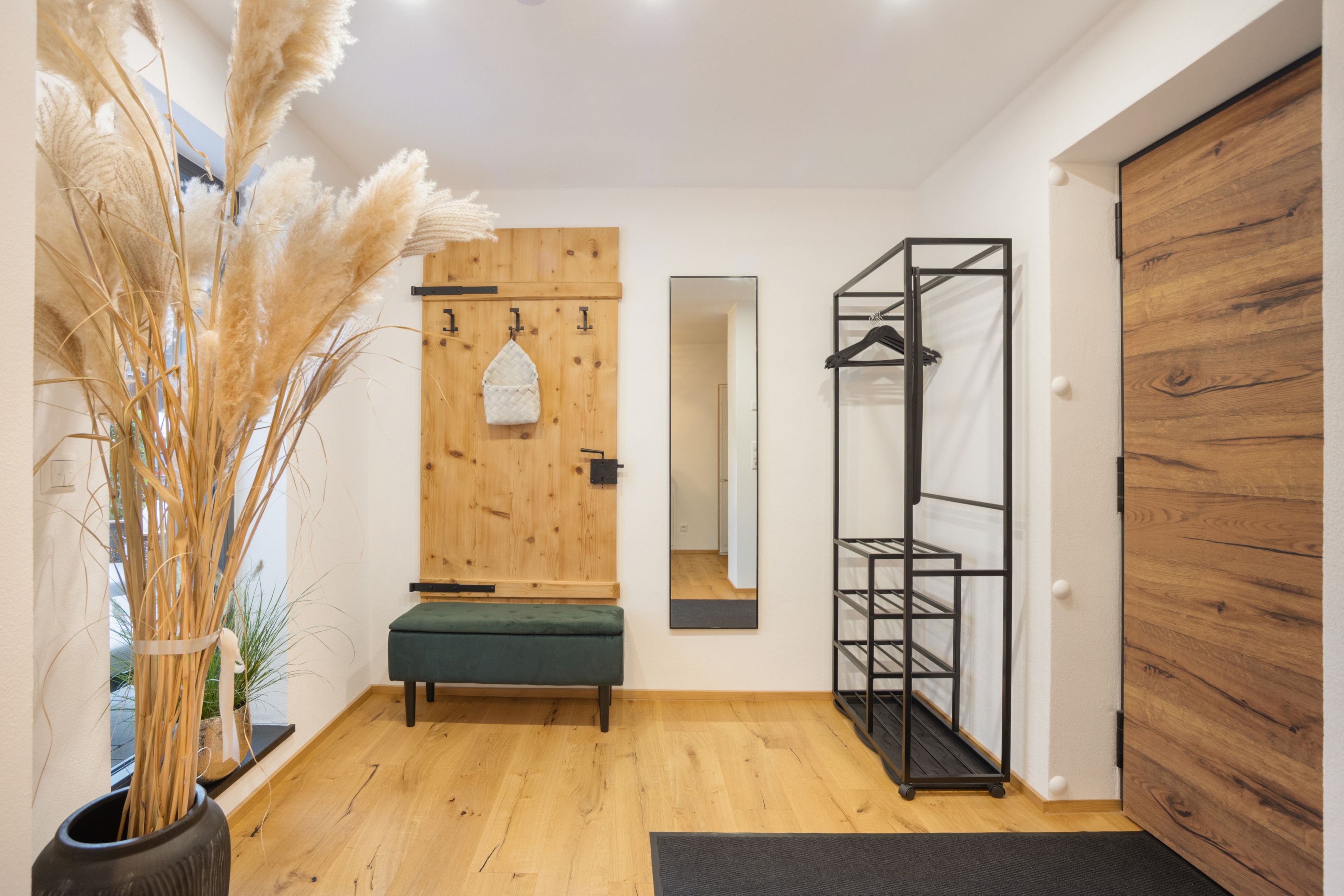 Ein Zimmer mit Holzboden, einer Bank, einem hängenden Kleiderhaken und einer Tür mit Spiegel.