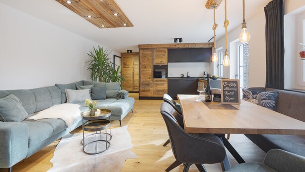 Un salon moderne avec un canapé gris, une table à manger en bois et une cuisine en arrière-plan.