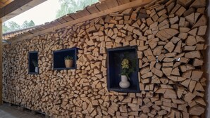 A wall of stacked firewood with three small windows, each containing a plant. - Allgäu 17 – Modern Alpine-Style Apartment (Leutkirch im Allgäu)