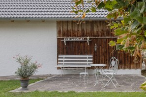 Une terrasse avec un banc blanc, une table en métal et des chaises, un pot de fleurs et une clôture en bois avec une pancarte.
