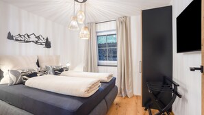 Une chambre moderne avec un grand lit, une fenêtre avec des rideaux, un téléviseur fixé au mur et un luminaire au plafond.