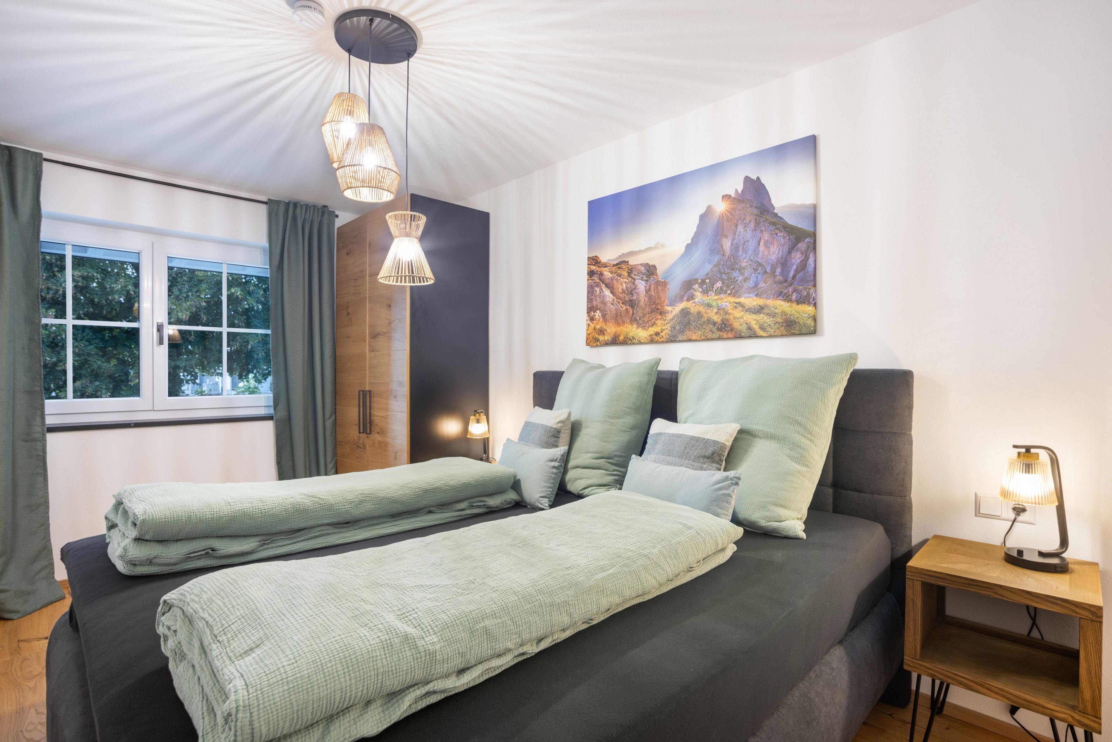 Ein Schlafzimmer mit einem Bett, einem Nachttisch, einer Lampe, einem Gemälde und einem Fenster mit Vorhängen.
