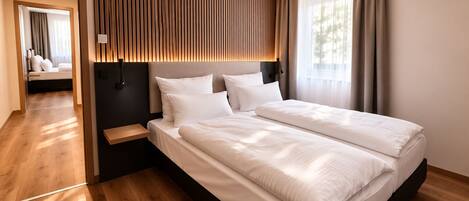 A modern hotel room with a large bed, wooden panel wall, and a view of the outdoors.