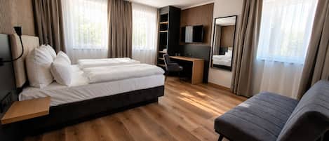 A hotel room with a bed, a desk, a chair, a sofa, and a TV.