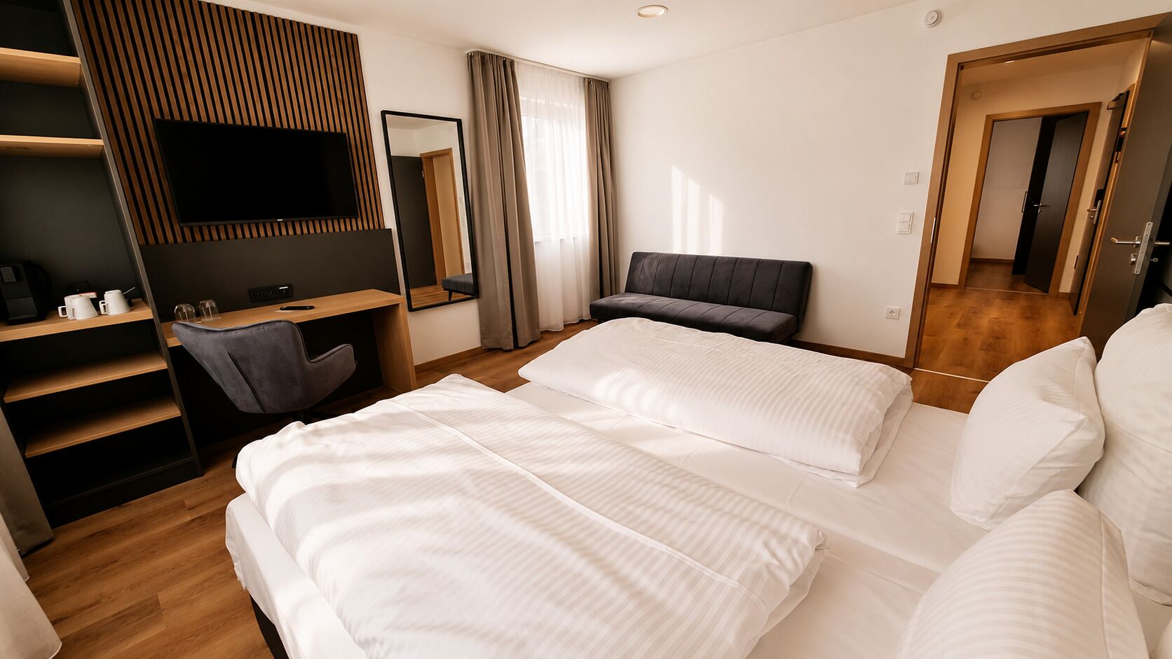 A hotel room with a bed, a desk, a chair, a TV, and a mirror.