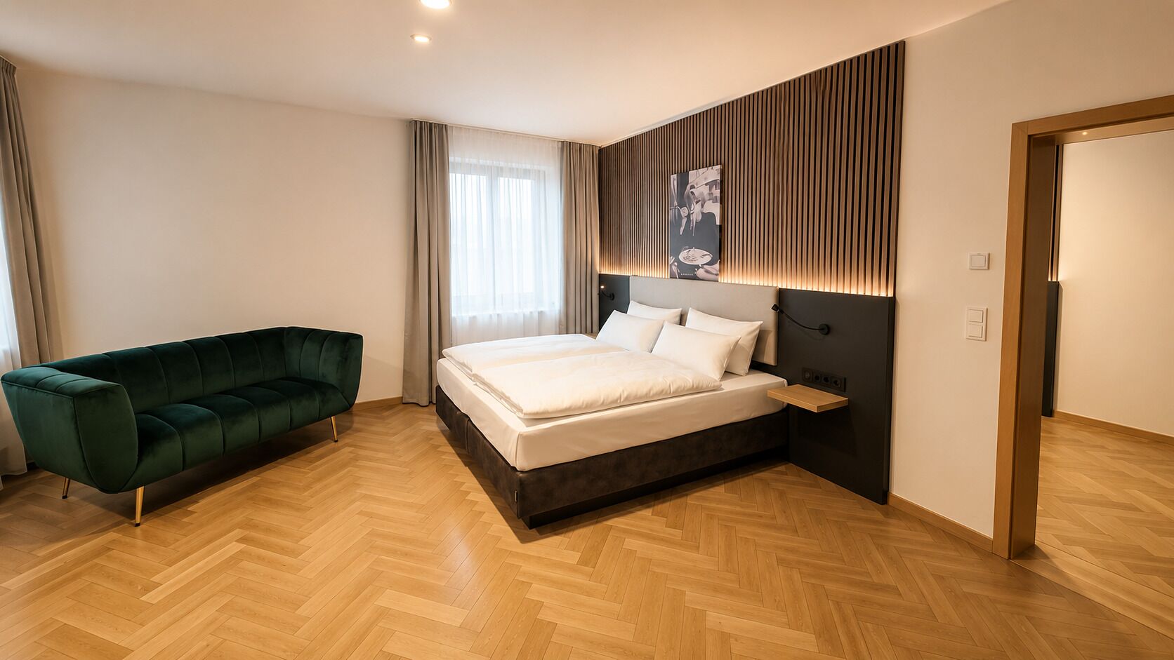 A modern bedroom with a bed, a green sofa, wooden flooring, and a wall-mounted artwork.