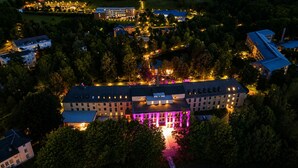 Una vista aerea di un hotel con diversi edifici, una struttura centrale con colonne illuminate e vegetazione circostante.
