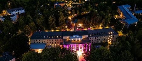 Vista aérea de un hotel con varias construcciones, una estructura central con columnas iluminadas y vegetación circundante.