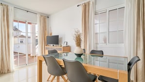 A modern dining area with a glass table, four chairs, a television, and a vase with dried plants. - Villa 'Bianca' with Sea Views, Wi-Fi, and Air Conditioning (Málaga)