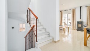 A staircase with wooden handrails, a dining area with a table and chairs, a kitchen with a stove, and a window with curtains. - Villa 'Bianca' with Sea Views, Wi-Fi, and Air Conditioning (Málaga)