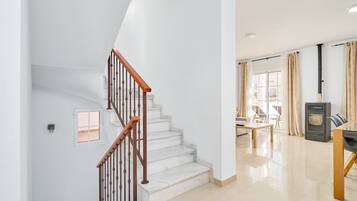 A staircase with wooden handrails, a dining area with a table and chairs, a kitchen with a stove, and a window with curtains.