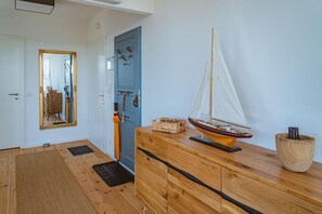 Un suelo de madera, una puerta azul con pomos, un aparador de madera, un velero modelo y un control remoto sobre un soporte de madera.