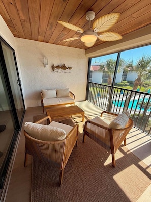 A balcony with wicker furniture, a ceiling fan, and a view of a swimming pool. - Updated Beachfront 2 Bedroom Condo on Longboat Key - Walking Distance to Shopping and Dining! (Longboat Key)