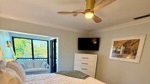 Een slaapkamer met een bed, een plafondventilator, een televisie en een schilderij aan de muur.