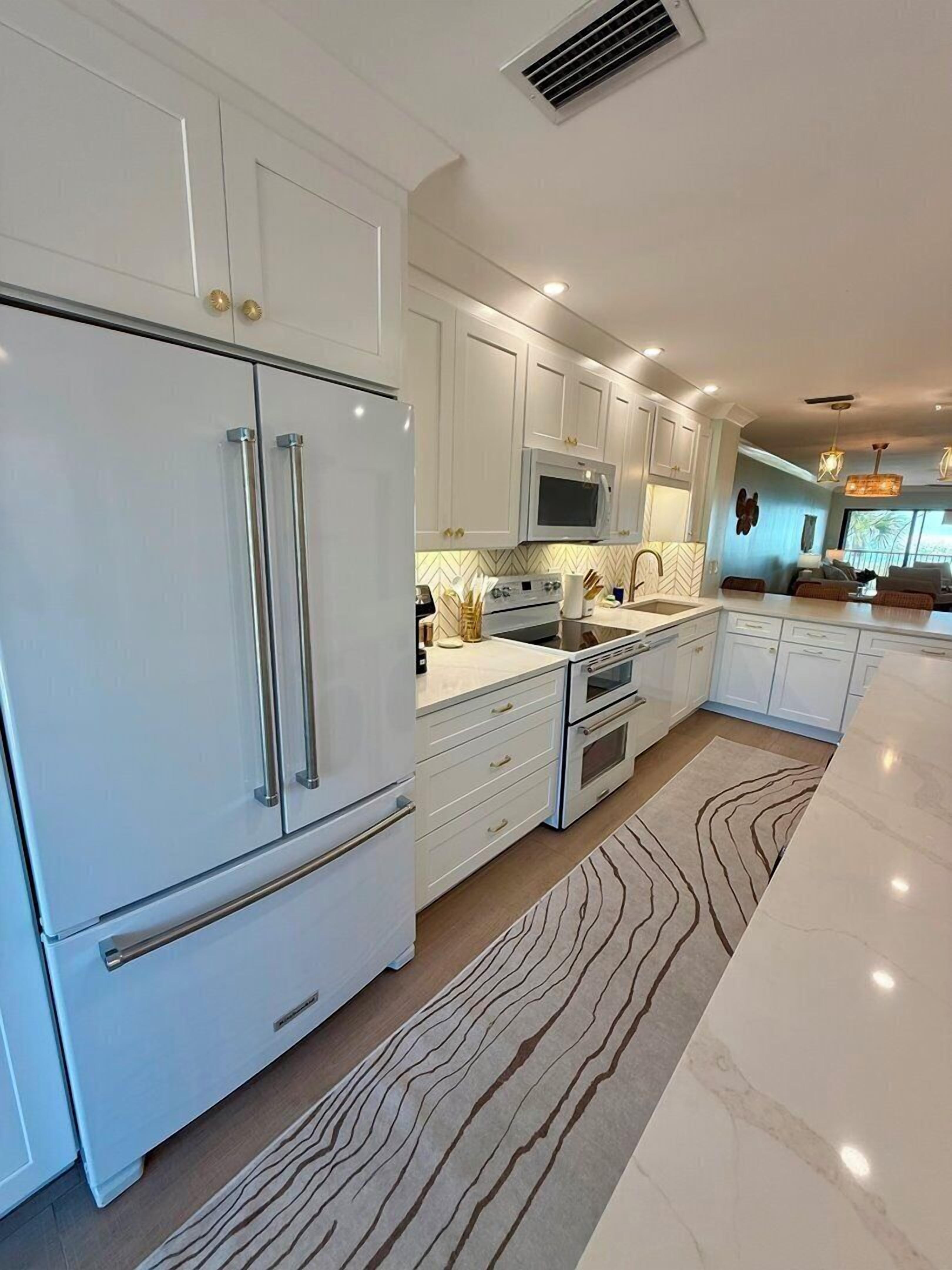 A modern kitchen with white cabinetry, stainless steel appliances, and a herringbone-patterned rug.