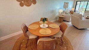 Een eetruimte met een ronde houten tafel, rieten stoelen en een geweven vloerkleed.