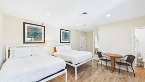 A hotel room with two beds, a small table with chairs, and artwork on the walls. - Rally Point Inn & Pub (Foxborough)