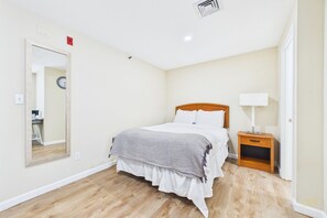 Un dormitorio con cama, mesita de noche, lámpara y espejo en la pared.